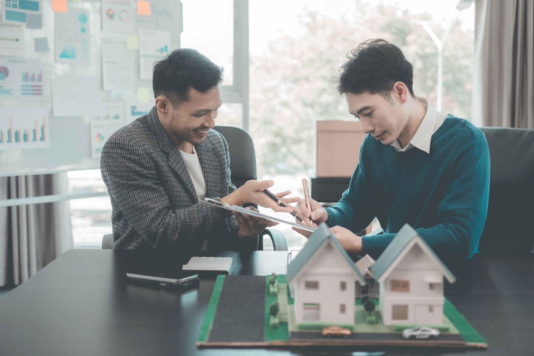 Investors reviewing a house model and documents during a real estate investment analysis meeting.
